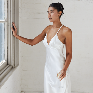 Bride dreaming whilst looking out the window in a satin maxi dress