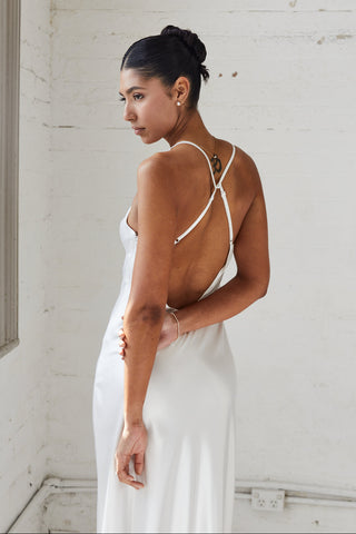 Woman in a white dress with thin straps standing against a white wall.